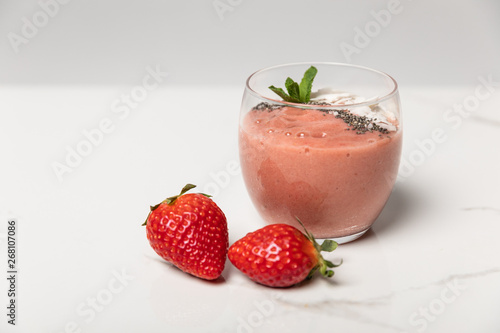 sweet ripe strawberries near tasty smoothie in glass on white