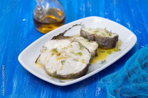 boiled fish with olive oil in white dish on blue wooden background
