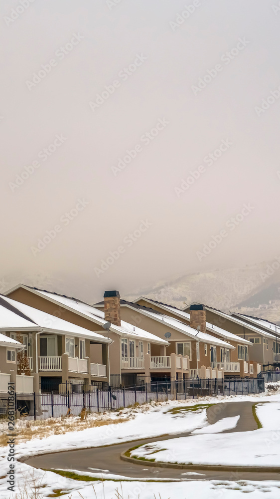 Vertical Facade of homes viewed against snow capped mountain and white sky in winter