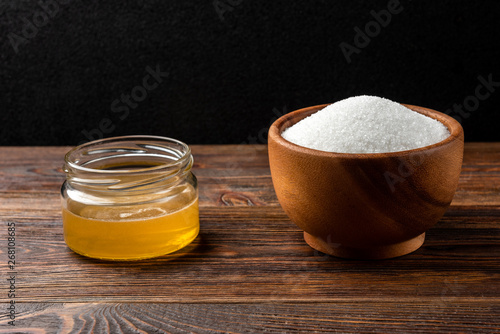 Honey and sugar on dark wooden background.