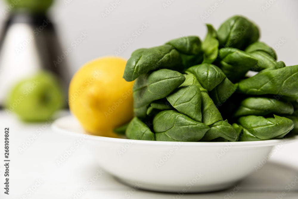 selective focus of green fresh spinach leaves near yellow lemon on white selective focus of green fresh spinach leaves near yellow lemon on white