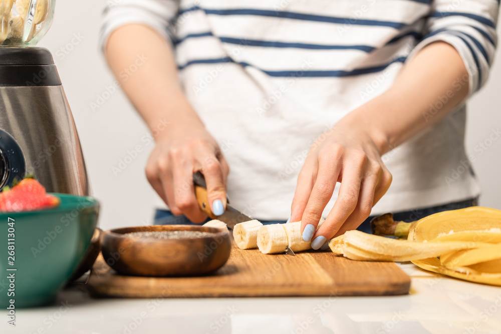 cropped view of woman cutting organic and ripe bananas on chopping board while standing on white cropped view of woman cutting organic and ripe bananas on chopping board while standing on white