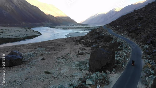 4k aerial following of motorbiker next to river in dry valley in Ladakh in India photo