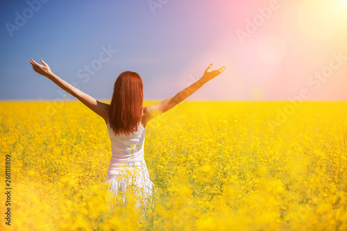 People freedom success concept. Happy woman in the field with flowers at sunny day in the countryside. Nature beauty background, blue sky and yellow flowers. Outdoor lifestyle.