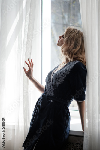 Beautiful young woman blonde in a blue robe by the window.