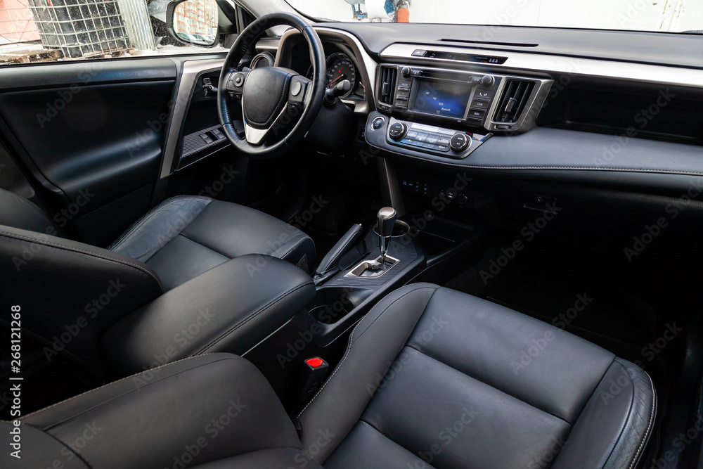 Comfortable front seats inside the car: the driver and passenger, tied with genuine black leather, modern interior design, the steering wheel covered with brown wood and a luxurious center console.