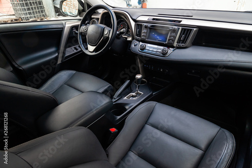 Comfortable front seats inside the car: the driver and passenger, tied with genuine black leather, modern interior design, the steering wheel covered with brown wood and a luxurious center console. © Aleksandr Kondratov
