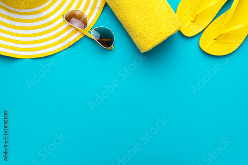 yellow beach accessories on turquoise blue background - sunglasses, towel. flip-flops and striped hat. summer is coming concept with copy space. holiday by the sea concept.