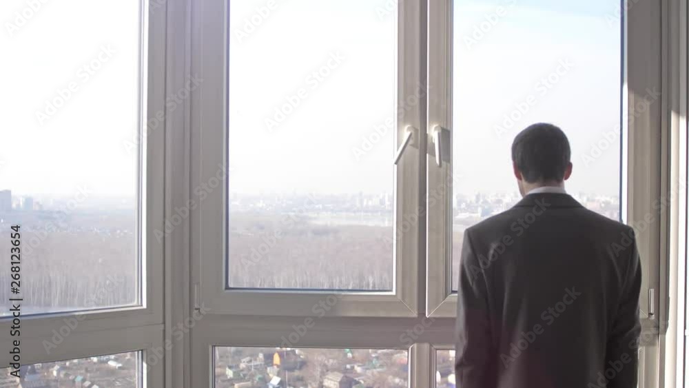 Back view of young successful businessman standing in front of windows looking into distance on the city. slow motion. 3840x2160 Back view of young successful businessman standing in front of windows looking into distance on the city. slow motion. 3840x2160