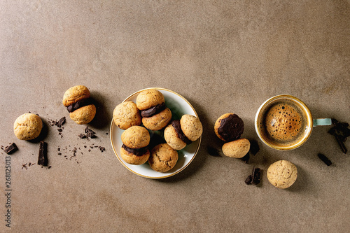 Baci di dama homemade italian hazelnut biscuits cookies with chocolate cream served in ceramic plate with cup of espresso coffee over brown texture background. Flat lay, space