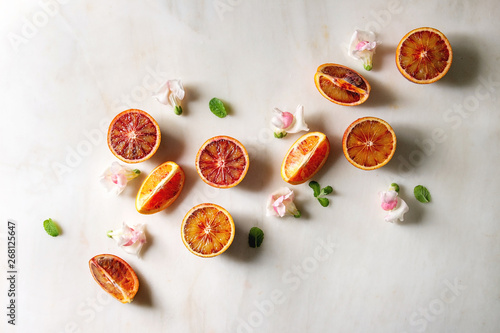 Group of fresh organic Sicilian blood oranges sliced and whole, edible flowers, mint leaves over white marble background. Flat lay, space