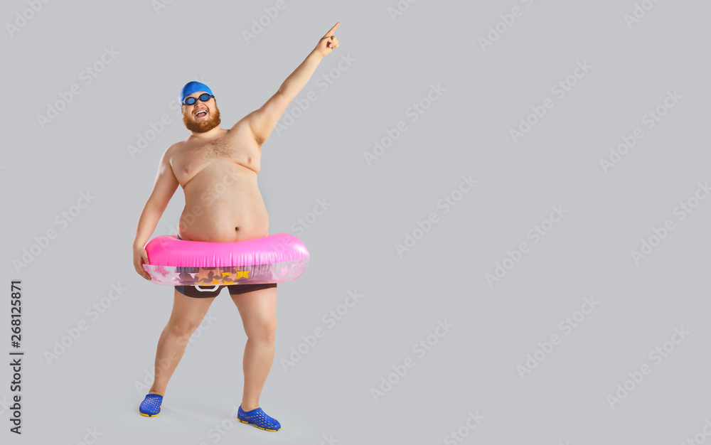 Fat funny man in swimming trunks with an inflatable ring on a gray  background. Stock Photo | Adobe Stock