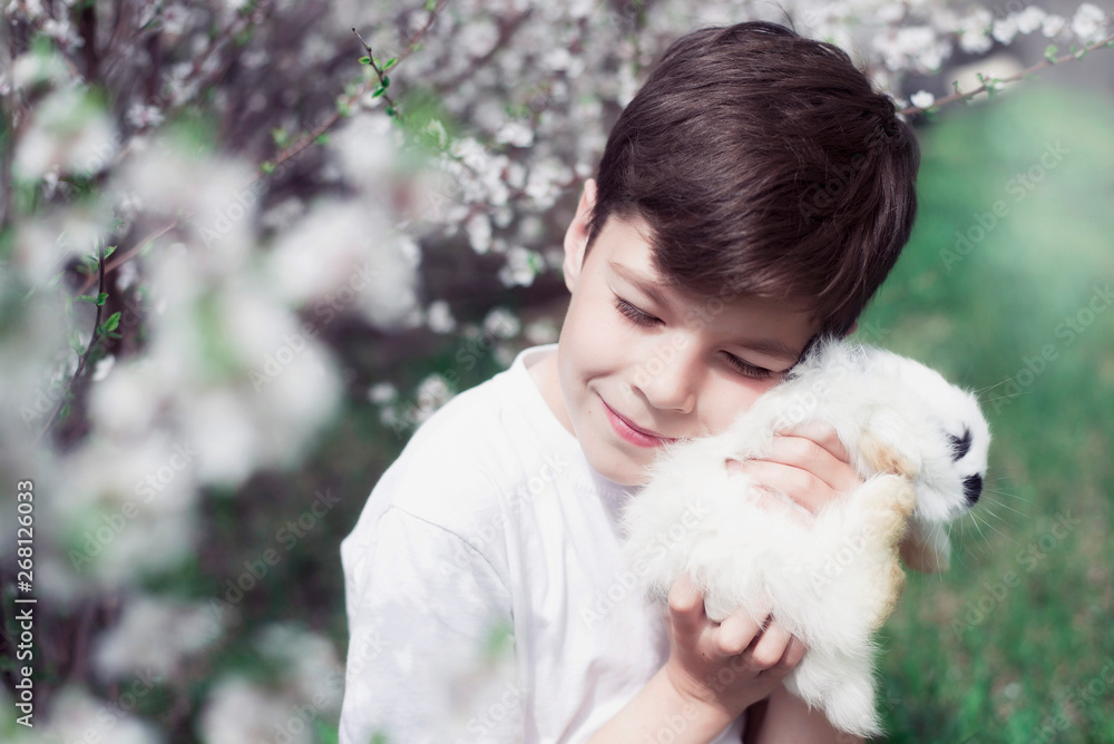 Handsome boy holding a fluffy, white rabbit in the hands against the background of flowering bushes. Handsome boy holding a fluffy, white rabbit in the hands against the background of flowering bushes.