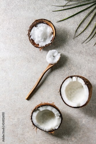 Organic vegan cold pressed coconut oil in coconut shell and wooden spoon over grey texture background. Healthy eating. Flat lay, copy space