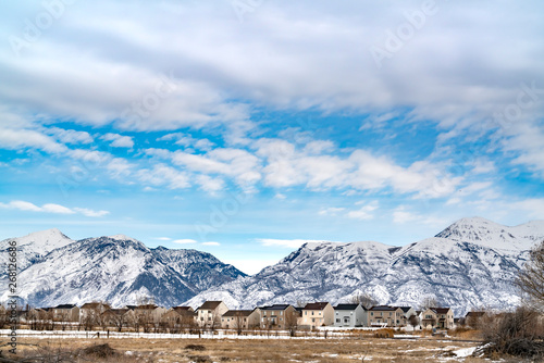 Beautiful blue sky with puffy clouds over homes and mountain in winter © Jason