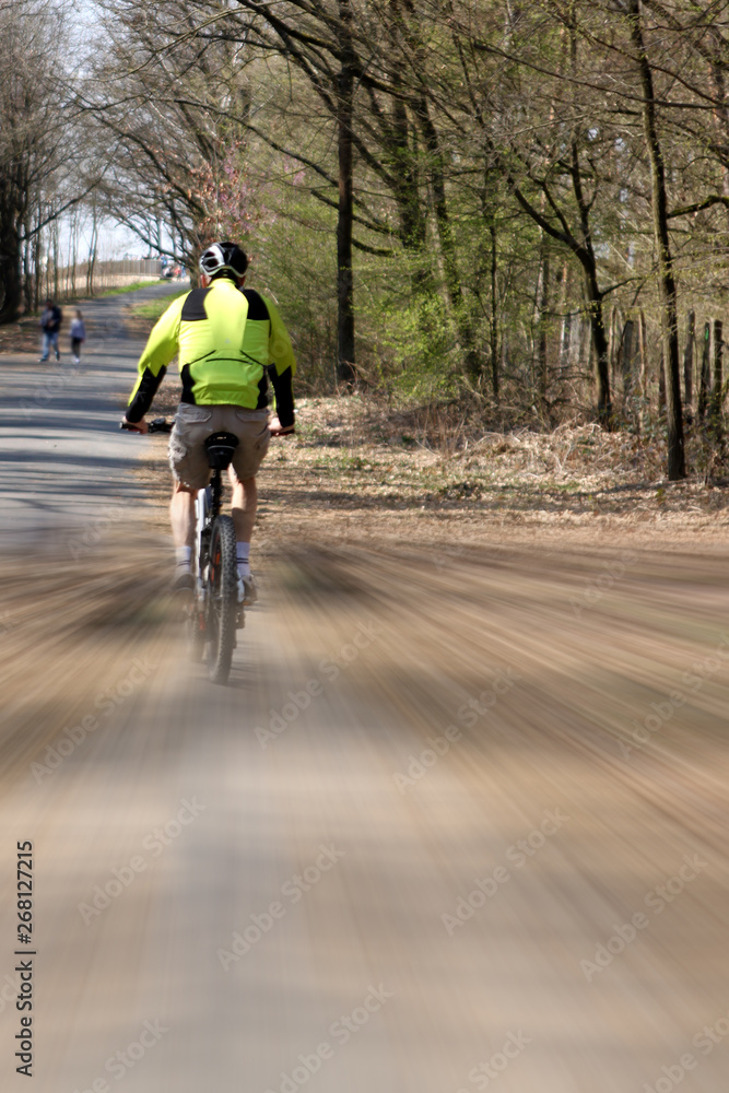 Obraz premium Cyclist rides along the park alley, artistically blurred image, speed lines