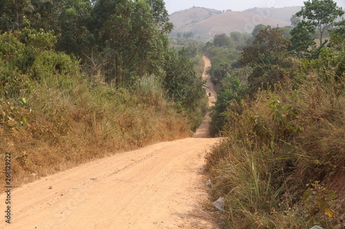 gruntowa droga biegnąca przez afrykański busz w pagórkowatym terenie photo