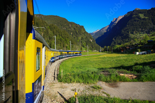 Yellow green train passes through a curved bend in the beautiful natural green grasslands and mountains in Wengernalp, an alpine meadow between Wengen and Kleine Scheidegg, Swiss Alps in Switzerland