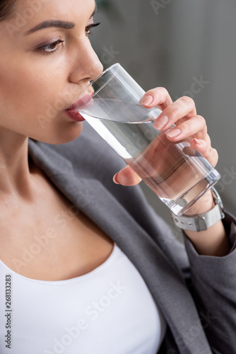 attractive woman drinking water from glass while suffering from heat on grey