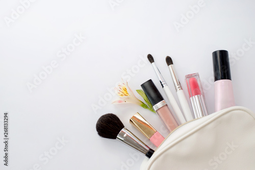 Woman flat lay makup background with cosmetics. Cream, lipstick, concealer, lipgloss and brushes. Top view on white background, copy space.