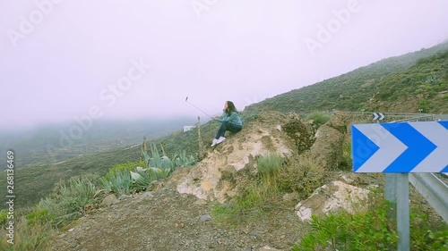 girl uses a selfie stick on the background of green rocks of a canarian volcano