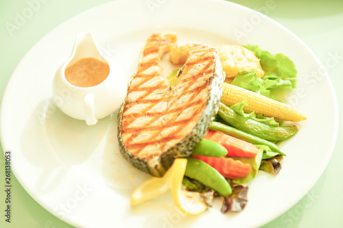 Grilled salmon with lemon and salad on white plate.