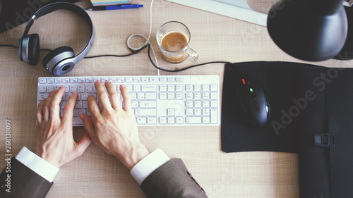 Top view on the office desk with coffee and computer keyboard and businessman's hands typing on the keyborad photo