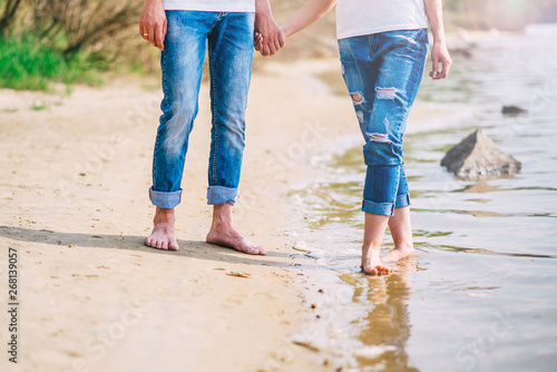 young barefoot couple walking along the beach. feet in the water summer