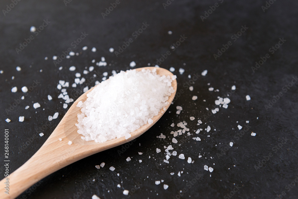 white coarse edible salt on a wooden spoon on a black surface white coarse edible salt on a wooden spoon on a black surface