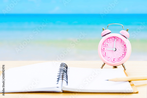 book and vintage clock with yellow on wooden platform beside tropical beach and blue sea on day noon light. back to school or summer camp fun party concept photo