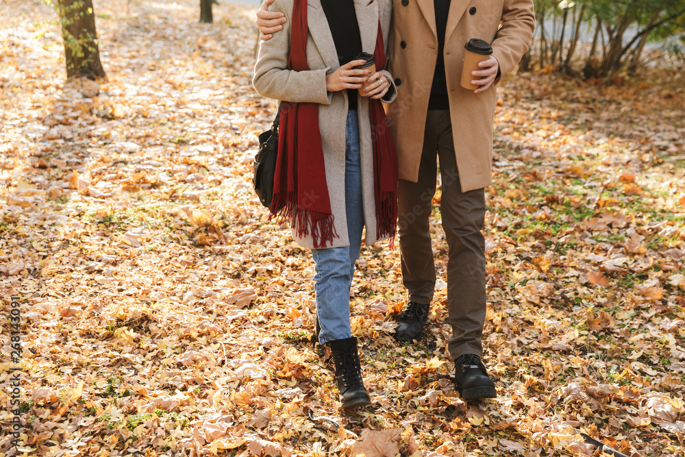 Cropped portrait of young couple drinking takeaway coffee while walking in autumn park