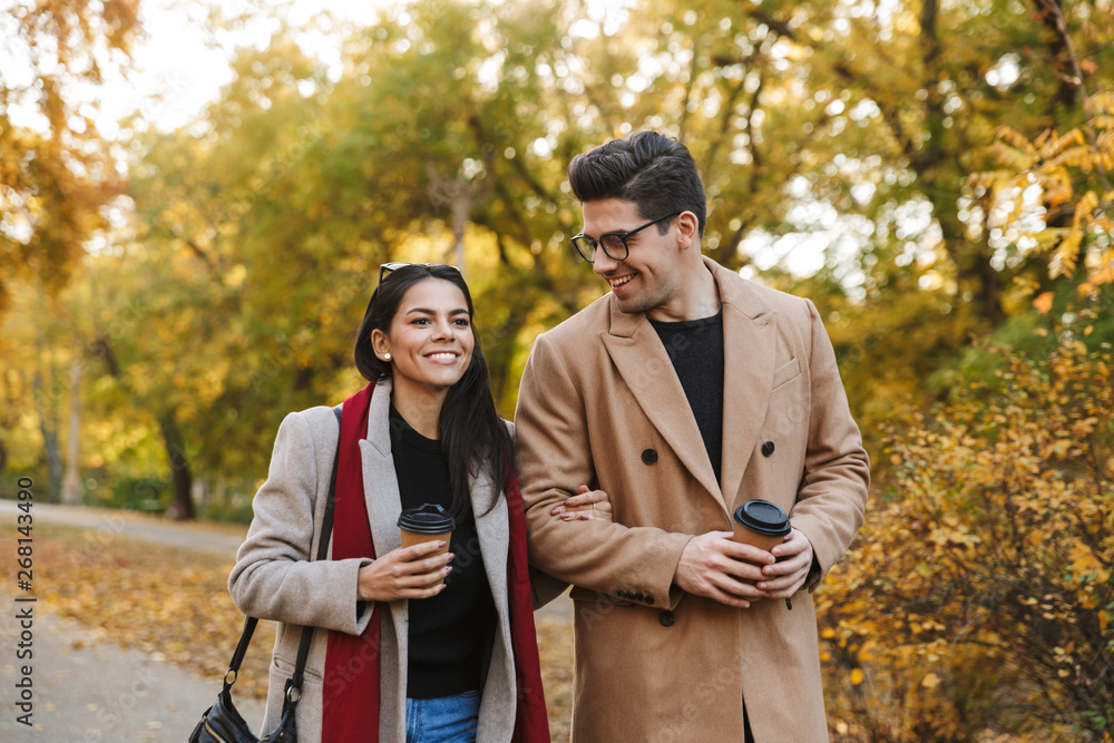 Portrait of european couple drinking takeaway coffee from paper cups while walking in autumn park Portrait of european couple drinking takeaway coffee from paper cups while walking in autumn park