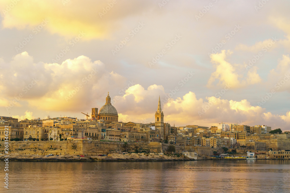 Fototapeta premium Valletta morning skyline with Basilica of Our Lady of Mount Carmel as seen from Sliema, Malta. Green plants landscape design garden foreground. Horizontal summer background or wallpaper.