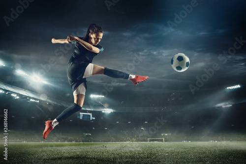 Młoda kobieta piłki nożnej lub piłkarz z długimi włosami w odzieży sportowej i butach kopiąc piłkę do bramki w skoku na stadionie. Pojęcie zdrowego stylu życia, sportu zawodowego, hobby, ruchu, ruchu