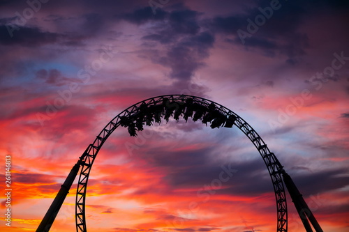 Silhouette of people having fun on a roller-coaster in an amusement park at sunset. Adrenalin concept. © belyaaa
