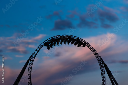 Silhouette of people having fun on a roller-coaster in an amusement park at sunset. Adrenalin concept.