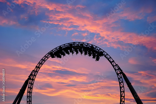 Silhouette of people having fun on a roller-coaster in an amusement park at sunset. Adrenalin concept.