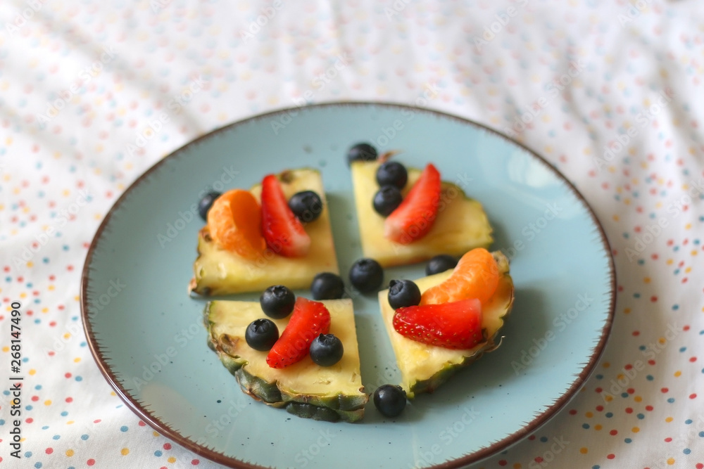 Plate with pineapple 'pizzas' - slices of pineapple with strawberries, tangerines and blueberries. Selective focus.