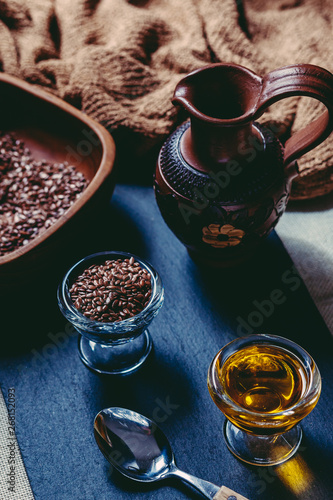 Linseed oil and flax seeds in glass sauceboats on a black stone. Jug of clay and a bowl of wood.