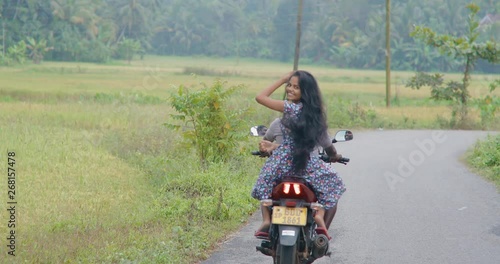 Sri Lankan couple riding a motorcycle on the road in the tropics. The girl with long beautiful and gorgeous hair looks very happy. real time. Shot on Canon 1DX mark2 4K camera photo