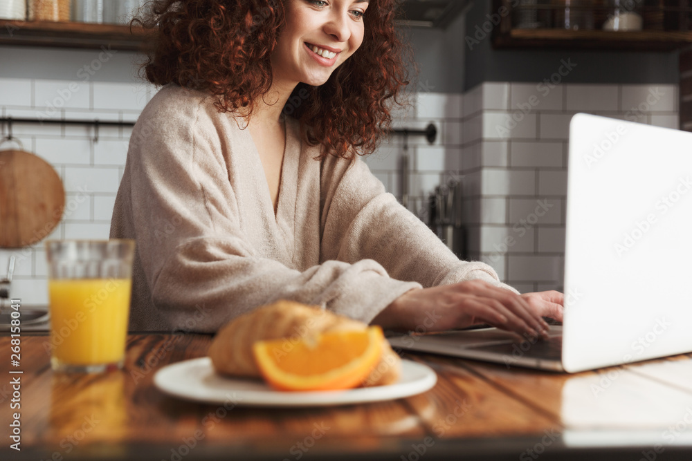 Portrait of smiling caucasian woman using laptop while having breakfast at home