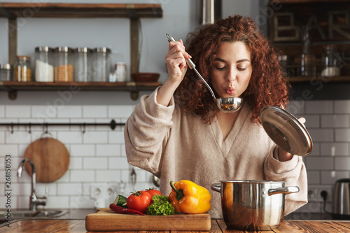 Photo of pretty caucasian woman holding cooking ladle spoon while eating soup at home photo