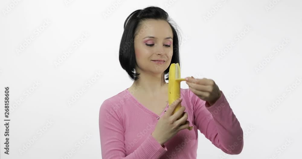 Young woman eating banana and says yum. Girl takes first bite and say wanna bite Young woman eating banana and says yum. Girl takes first bite and say wanna bite