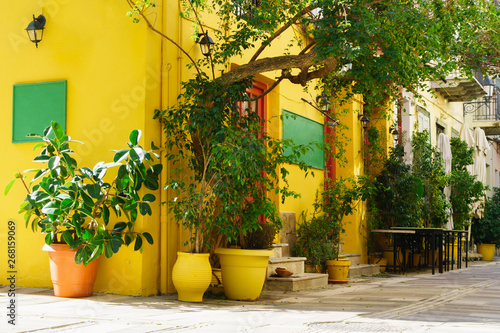 Traditional cozy greek street with yellow cafe walls, flowers in pots and green desk in city Nafplio, Greece. Mediterranean summer touristic destination.