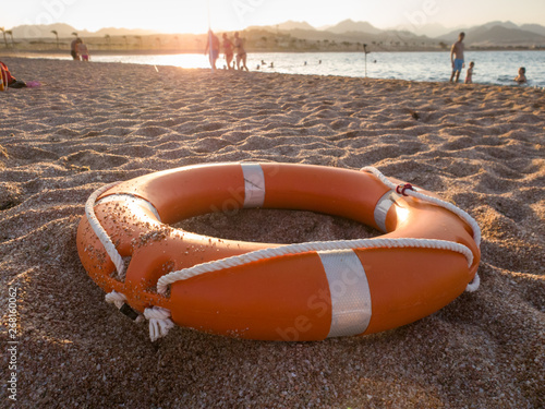 Closeup image of red plastic life saving ring on sandy sea beach at sunset light