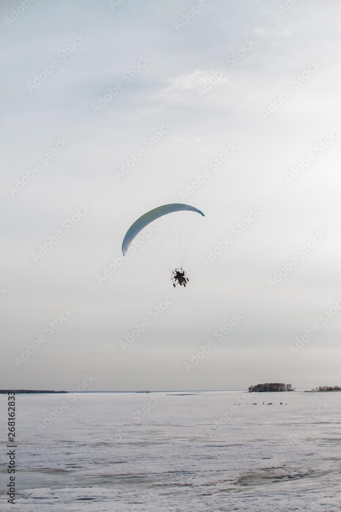 Paraglider with motor flies over the sea, which is covered with ice and snow. Free flight in winter Paraglider with motor flies over the sea, which is covered with ice and snow. Free flight in winter