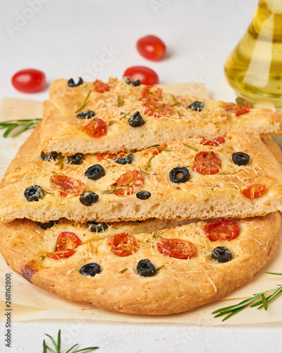 Focaccia, pizza, chopped italian flat bread with tomatoes, olives and rosemary. Vertical, side view.