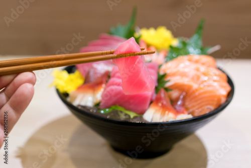 Chopsticks with Tuna sashimi with Mixed sliced fish sashimi on ice in black bowl. Sashimi Salmon Tuna Hamachi Prawn and Surf Calm set, raw fish, japanese food in Asian restuarant.