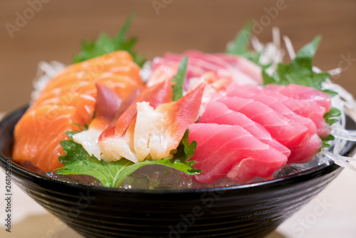Mixed sliced fish sashimi on ice in black bowl. Sashimi Salmon Tuna Hamachi Prawn and Surf Calm set, raw fish, japanese food in Asian restaurant.