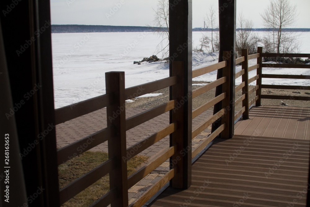 Veranda of dark brown timber. Beautiful sea view covered with ice and snow. Country rest.